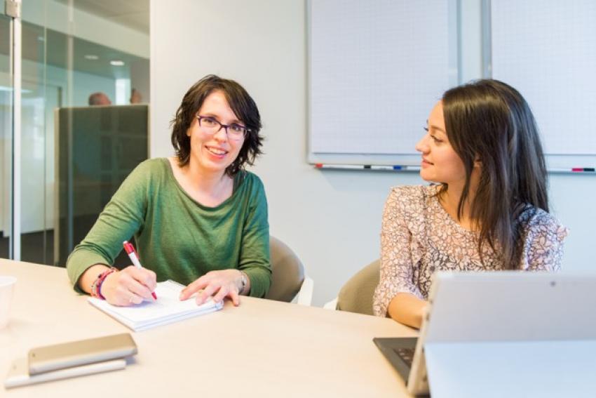 afbeelding van 2 collega's aan een tafel in overleg